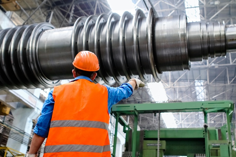 A man wearing an orange hard hat inspecting a large piece of machinery